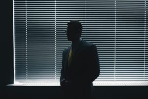 Silhouetted senior executive in suit and tie contemplating against blinds, representing strategic thinking for an impact-driven resume.