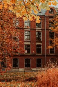Red brick university building facade framed by vibrant orange and golden autumn leaves, symbolizing the Fall intake period for international students.