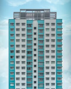 A high-rise residential complex with dual tone of white and turquoise/teal. The building is against the backdrop of a blue sky.