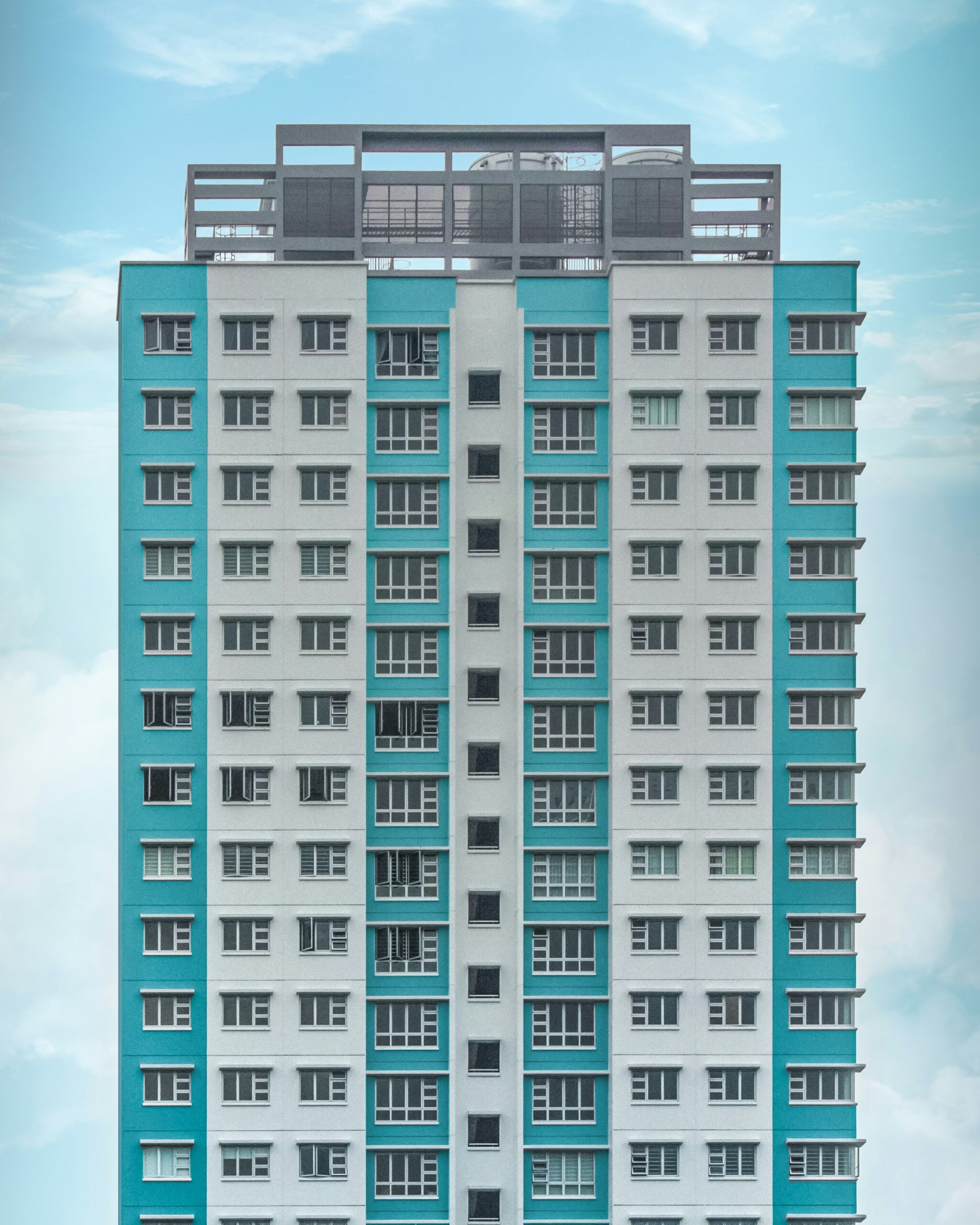 A high-rise residential complex with dual tone of white and turquoise/teal. The building is against the backdrop of a blue sky.